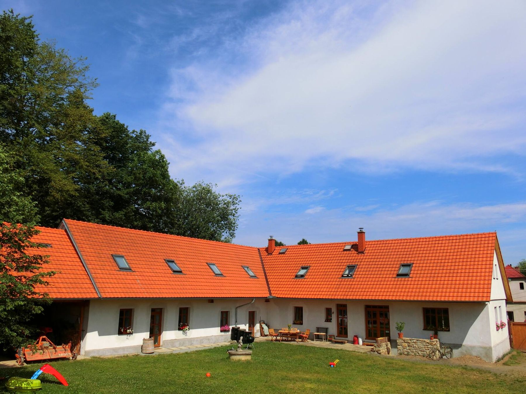 Bílý statek s oranžovými střechami a trávníkem pod modrým nebem